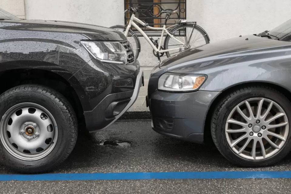 Two grey cars parked head to head at a curb with a white bike in background